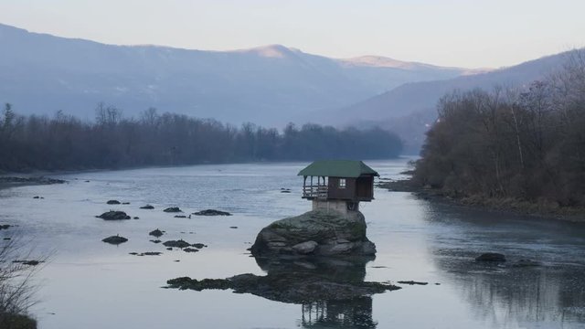 A Tiny Home Built on a Rock on the River Drina in the Small Town of Bajina Basta, Serbia. Filmed During Morning Hours at Sunrise. Reflections Can be Seen on Blue River Water