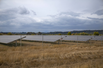 Front, angular view of  solar panels in a field of brown grass with clouded sky