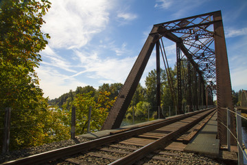 Picturesque angular view of iron and wood railroad trestle train tracks and bridge canopy, with green lush trees and vegetation, blue sky with wispy white clouds, daytime - Oregon USA