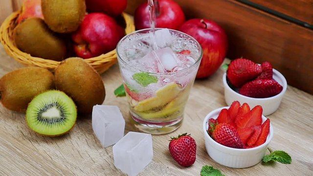 pouring soda water for making detox water fruit with apple wiki stawberry and ice in glass on wood background