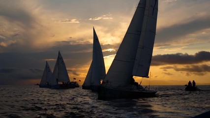 Slomotion shot of silhouettes of sailing yachts on a sailing regatta during sunset