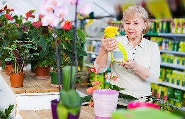 Adult female gardener is choosing substances for flowers in greenhouse.