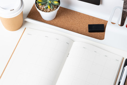 top view of open calendar planner with modern office stationery and take away coffee cup on white desk in office.mock up space of organizer table notebook.