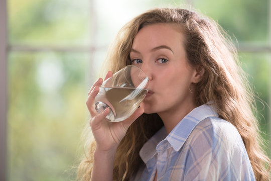 Healthy young woman drinking water at home