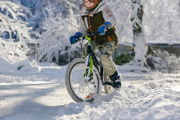 Fototapeta na wymiar Little boy riding bicycle on snowy winter road
