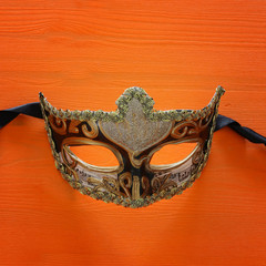 Halloween holiday minimal top view image of venetian elegant mask over orange wooden background.