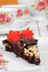 Piece of delicious homemade brownie cake with strawberries and tea set on white table. Selective focus