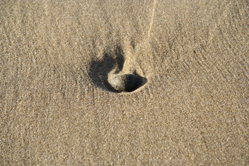 A small rock submerged into a sand on a beach after a low tide with water streams texture around