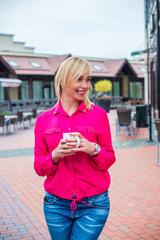 Portrait of elegant mature female who is enjoying of lunch with coffee in cafe with good mood. Lovely middle-aged blond woman with a beaming smile sitting in cafe having coffee 