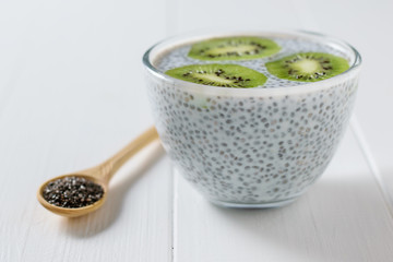 Glass bowl with milk Chia seed pudding and wooden spoon on white wooden table.