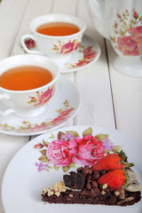 Piece of delicious homemade brownie cake with strawberries and tea set on white table. Selective focus