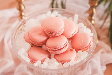 pink macaroons decorated with edible gold and white marmalade in the form of stones in a transparent candy box. Details of a beautiful pastel table setting