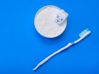 A cheerful tooth figure in a jar with tooth powder and a toothbrush on a light blue background. The view from the top. Flat lay.