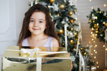 Girl in Christmas hats is sitting with gift boxes in his hands with the joy of a surprise.