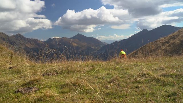 4k sport footage, one man on electric mountain bike cycling down meadow grass pasture high up in european alps mountain panorama sunny day in autumn
