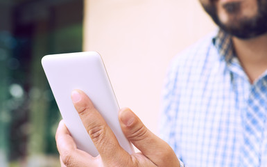 Cropped image young man sitting at the table with cup of coffee and smart phone, man's hands typing message on phone touch screen while sitting on balcony terrace.