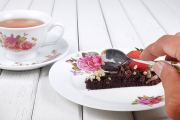 Close-up of a hand holding a spoon slicing into a delicious homemade brownie cake with strawberries