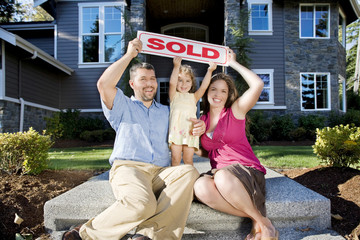 family with a sold sign in front of their new home