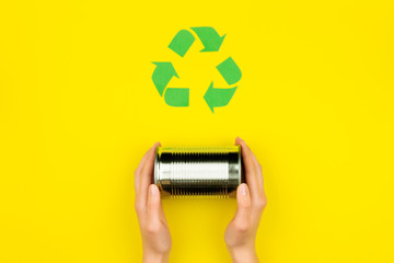Human hands with metal aluminium can jar on yellow background with green recycle reuse arrow sign...