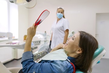 Woman patient looking in the mirror at the teeth, sitting in the dental chair
