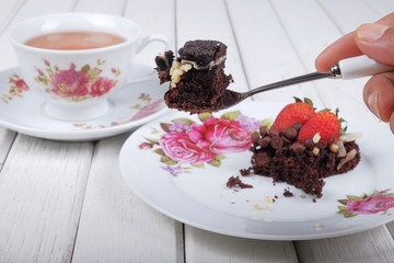 Close-up of a hand holding a spoon slicing into a delicious homemade brownie cake with strawberries
