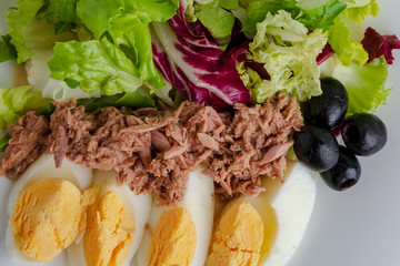 Tuna salad with egg, black olives and greens close up
