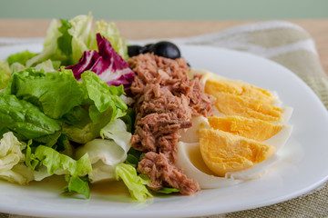 Tuna salad with egg, black olives and greens close up