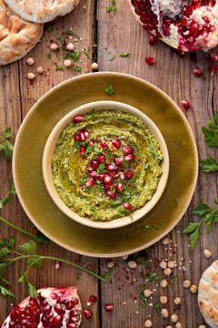 Hummus. Herbal hummus with the addition of pomegranate seeds, parsley, olive oil and aromatic spices in a ceramic pot on a wooden rusty table, top view. A healthy and delicious vegan dish
