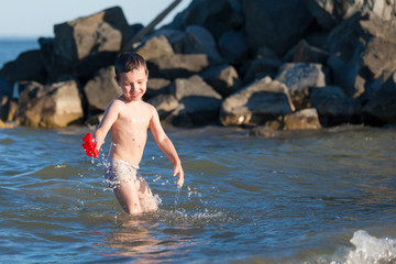 Happy boy playing in the sea. Kids having fun outdoors. Summer vacation and healthy lifestyle concept.