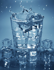 Pouring ice cube into drink glass of water. splashing of water.