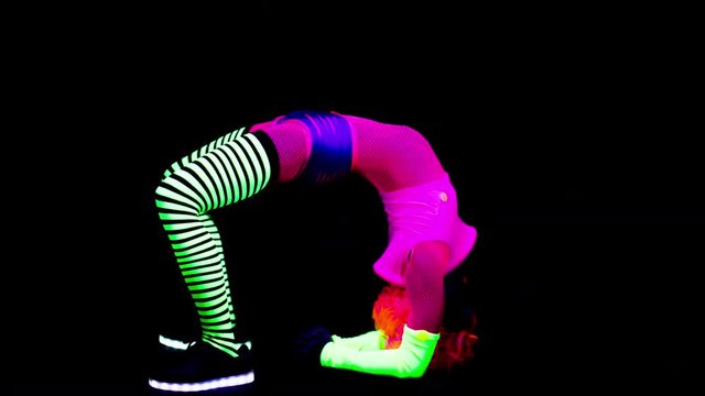 amazing female yoga instructor doing back bend poses wearing fluorescent clothing under UV black light