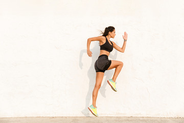 Full length image of young sportswoman 20s in sportswear working out and running, along wall
