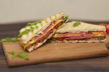 Grilled sandwiches with ham, cheese, tomatoes and arugula salad on a dark background. Delicious breakfast.