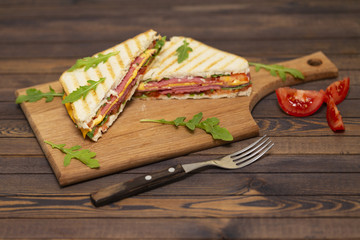 Grilled sandwiches with ham, cheese, tomatoes and arugula salad on a dark background. Delicious breakfast.