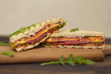 Grilled sandwiches with ham, cheese, tomatoes and arugula salad on a dark background. Delicious breakfast.