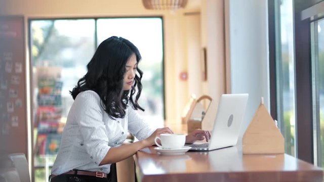 Young Asian pensive freelancer woman enthusiastically working or writing using laptop pc