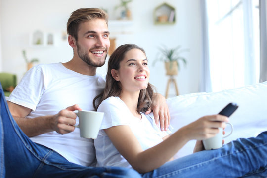 Young Loving Couple On Sofa At Home Watching Tv And Laughing.