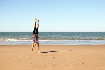 Young woman doing a handstand on a beach in summer