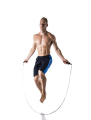 Shirtless muscular young blond man jumping or skipping rope in studio shot, isolated on white