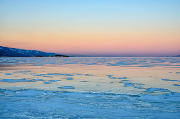 Fototapeta premium Blue ice of Baikal lake under pink sunset sky