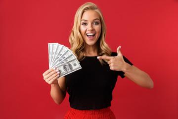 Excited woman holding money isolated over red background.