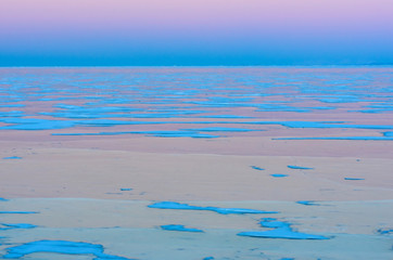 Obraz premium Blue ice of Baikal lake under pink sunset sky