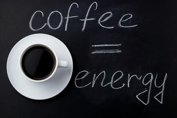 top view black coffee on a black background with inscription coffee equals energy made with white chalk