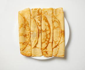 Crepe closeup, heap of thin pancakes on a dish, white background