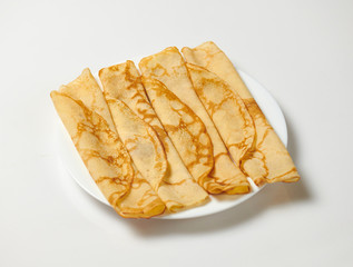 Crepe closeup, heap of thin pancakes on a dish, white background