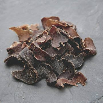 Biltong (protein snack) on a black slate tile, this is a traditional food snack that can be found in South Africa.This image has selective focusing. 