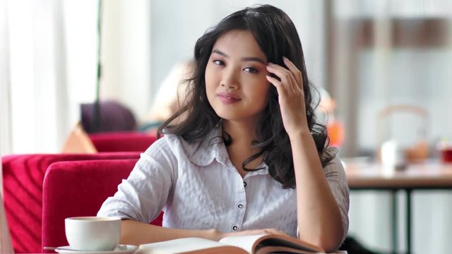 Asian young female student enjoying free time sitting with book and cup of coffee