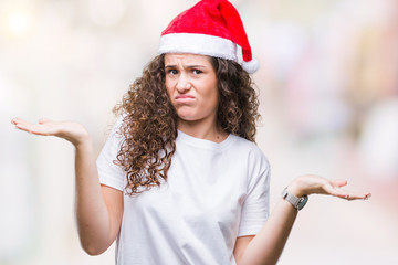 Young brunette girl wearing christmas hat over isolated background clueless and confused expression...