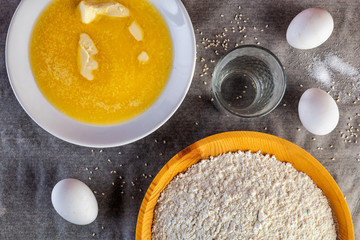 Flat lay. A set of fresh ingredients to make a soft fluffy dough: butter, flour, egg, a glass of water. The process of making dough for bread, muffin, pizza, buns and hamburgers on the kitchen table