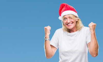Obraz premium Middle age blonde woman wearing christmas hat over isolated background very happy and excited doing winner gesture with arms raised, smiling and screaming for success. Celebration concept.